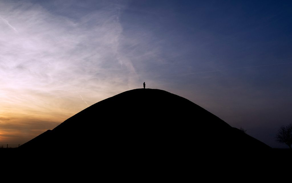 Silhouette of alone man standing on the top of a hill during sunset.