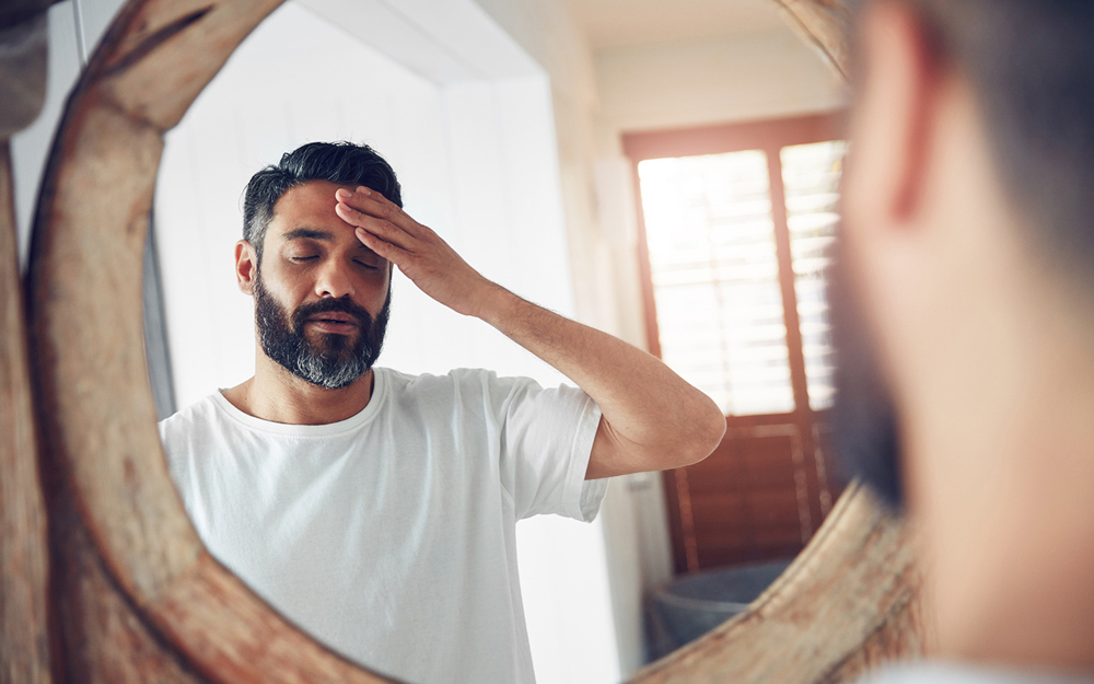 A tired man with a beard looking into the mirror wondering if he has adrenal fatigue.