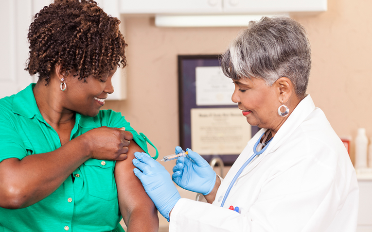Older female healthcare worker gives an African-American woman a flu shot.