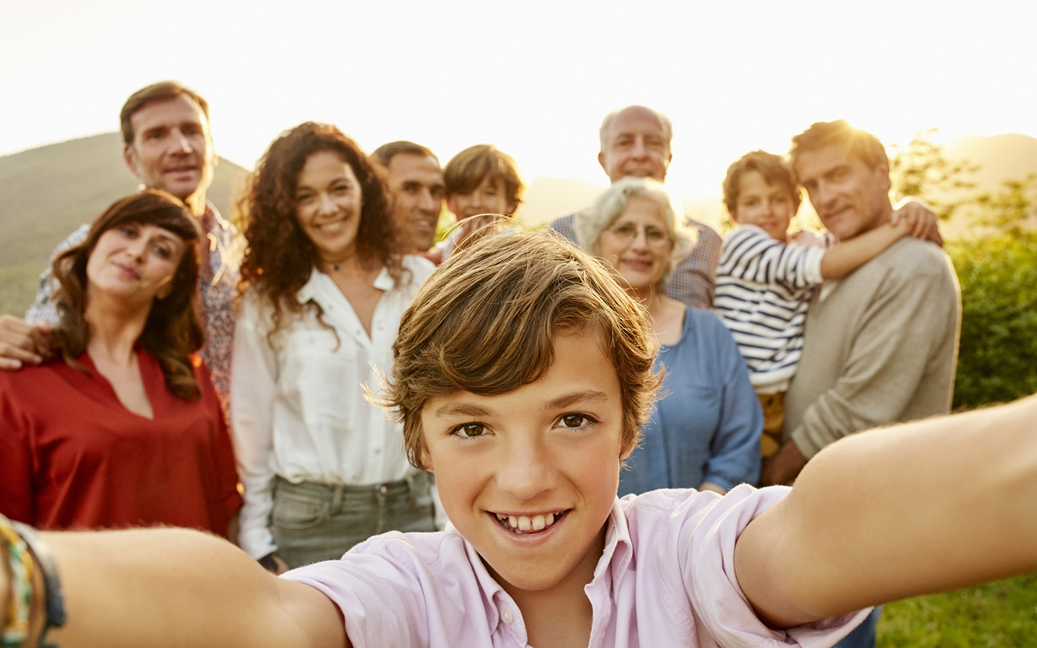 A young boy shoots a selfie with his family in the background.