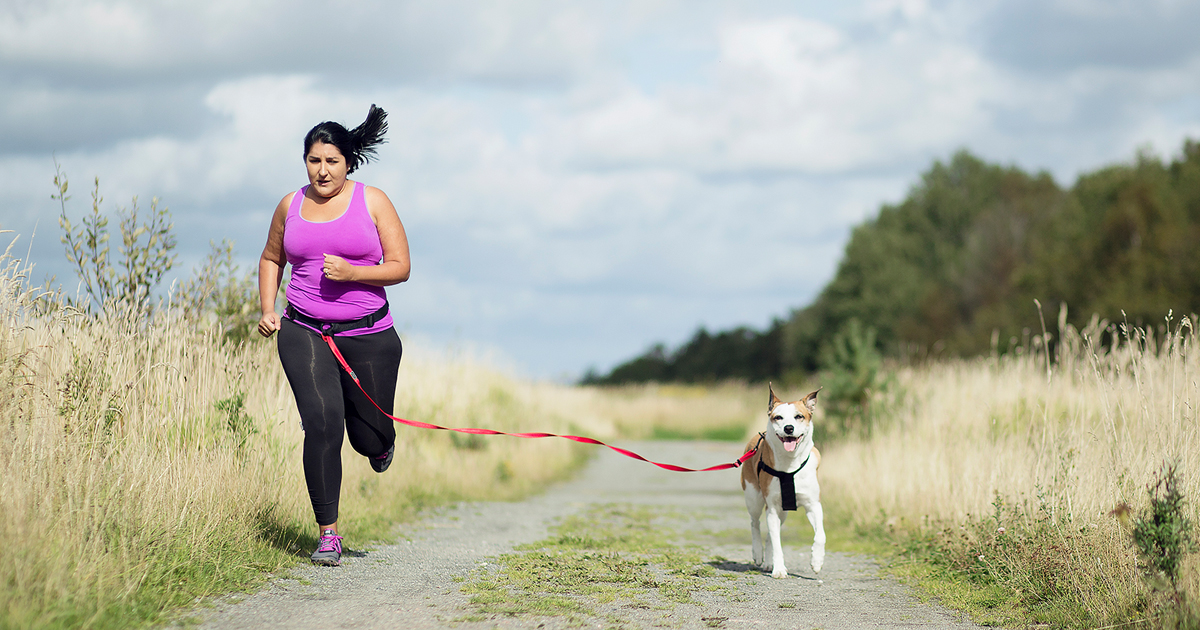 A middle-aged woman running on a trail with a dog.