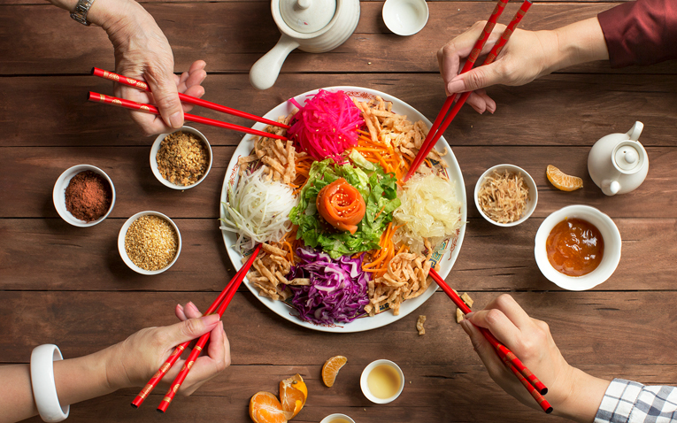 Four people holding chopsticks sharing a plate of food.