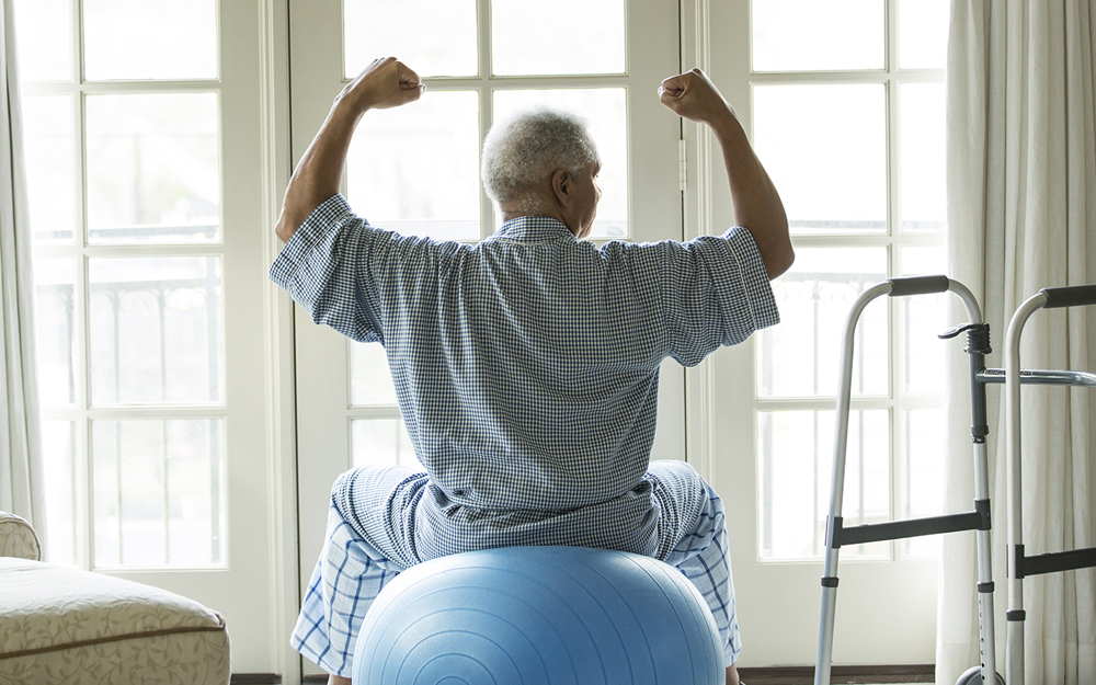 Elderly man sitting on top of a yoga ball.