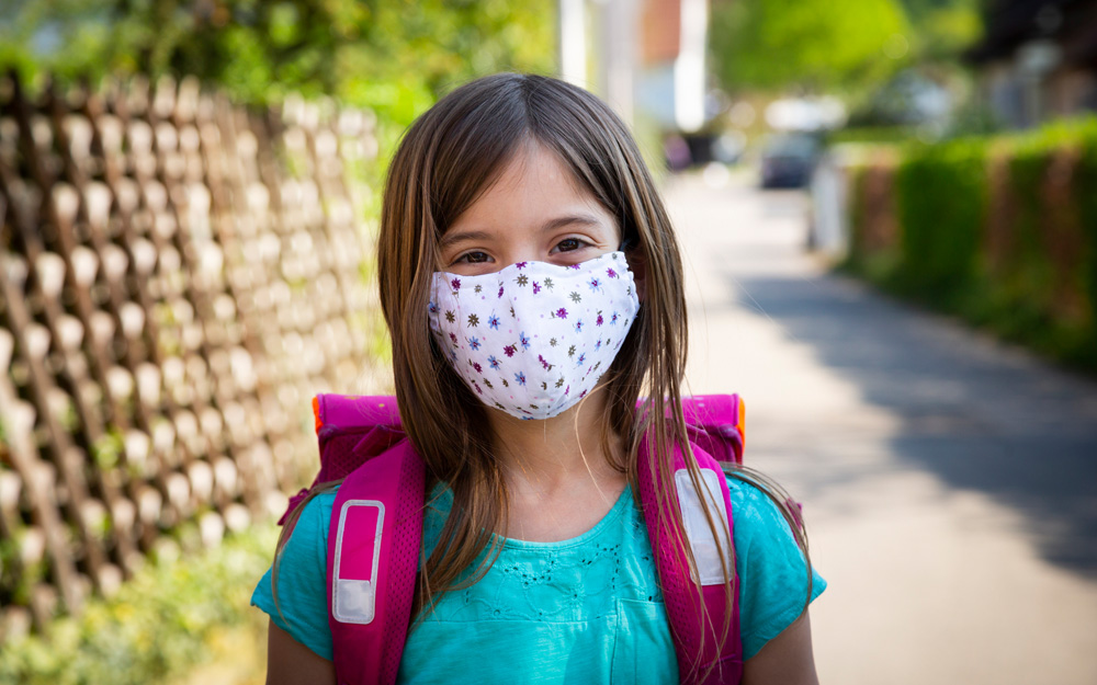 A young girl in a mask returning to school during the COVID-19 pandemic.