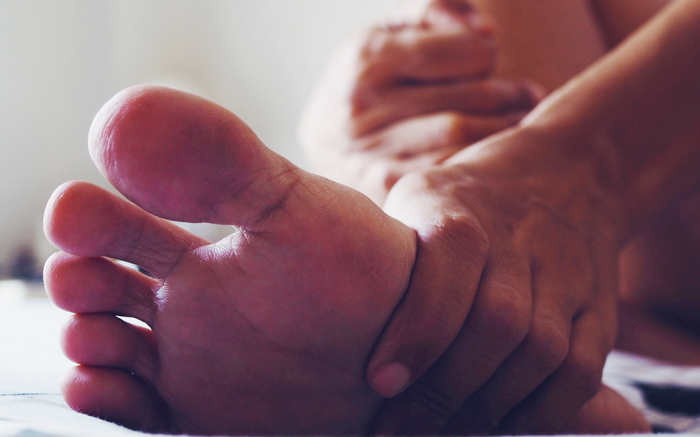 A person rubbing their feet after suffering a foot injury at home by not wearing house shoes.