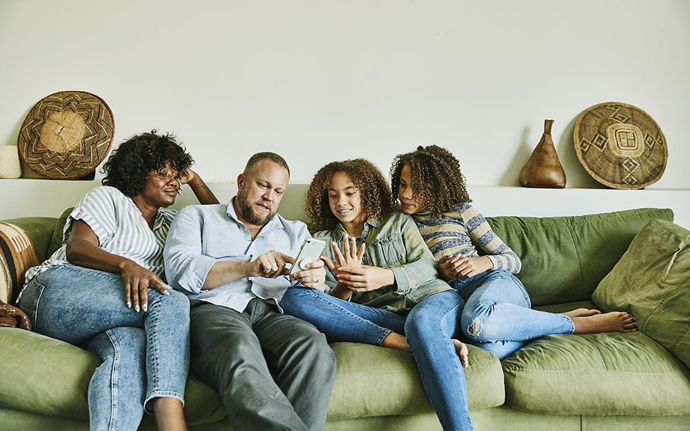 Family sitting on couch in living room looking at smart phone