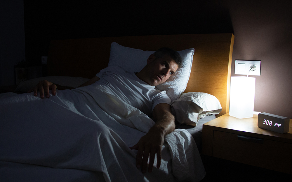 Man in bed staring at the clock.