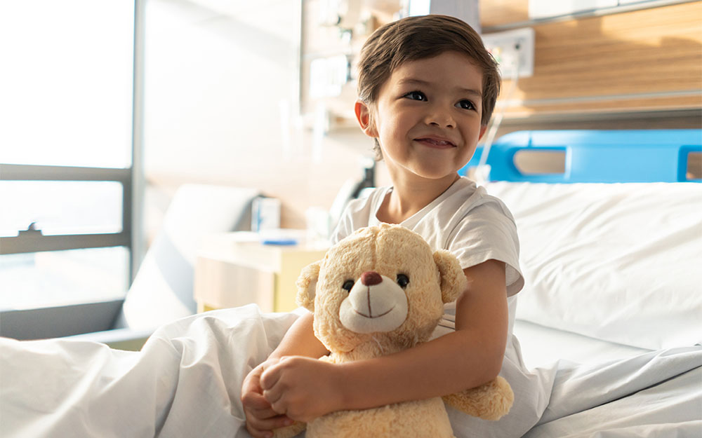 Happy pediatric patient at the hospital holding a teddy bear