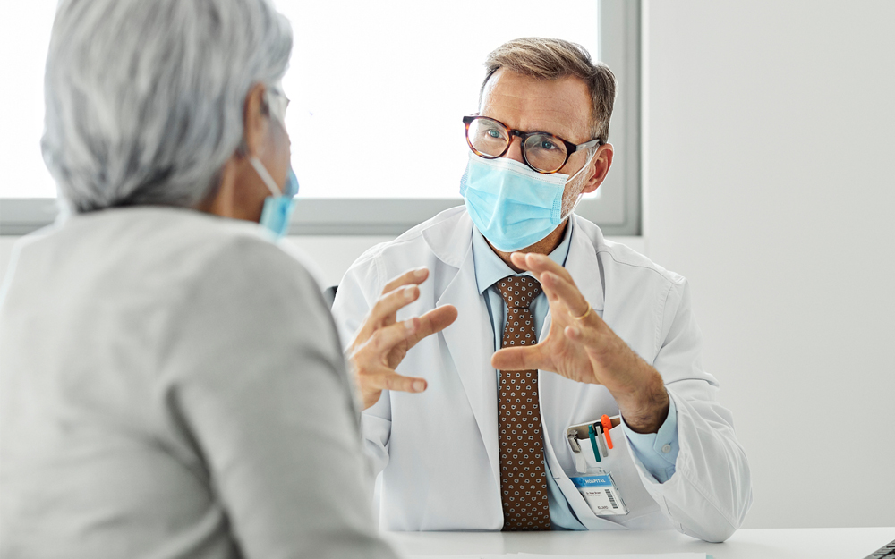 A doctor talking to a patient in office during the COVID-19 pandemic.