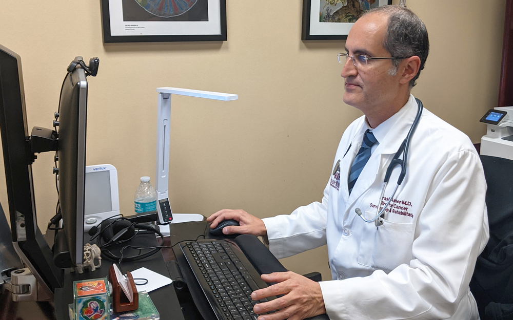 Dr. Arash Asher at the computer connecting cancer patients virtually during the COVID-19 pandemic. 