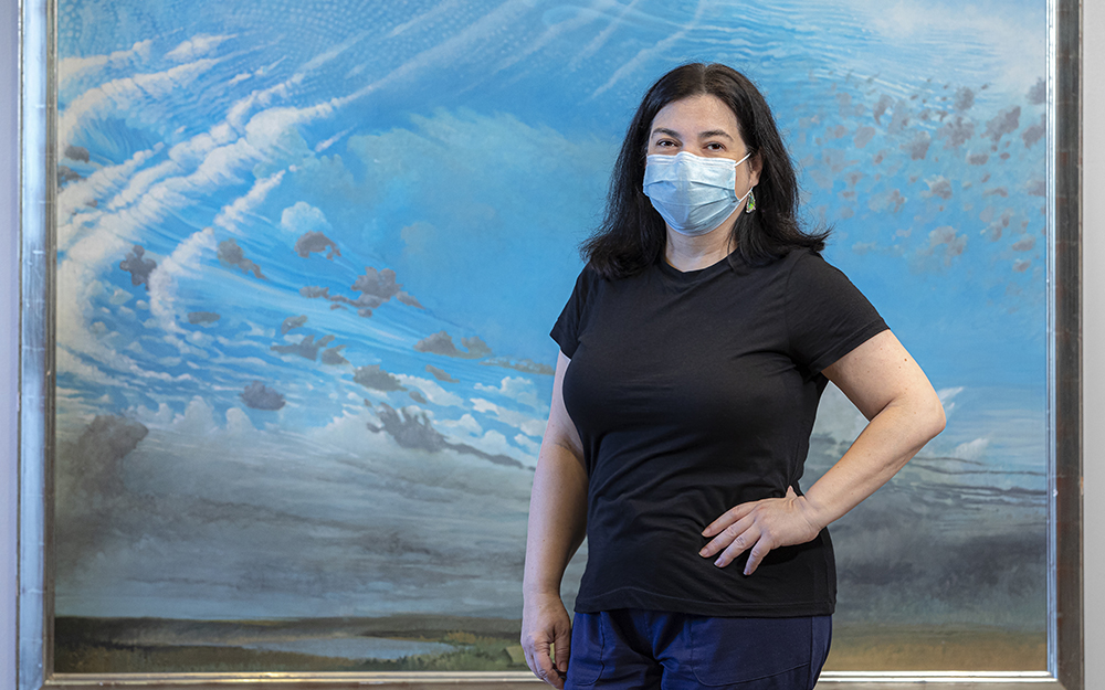 Telma Thomassian-Lopez, Sr. Administrative Assistant of Office of Licensure, Accreditation and Regulation at Cedars-Sinai standing in front of Peter Zokosky, "Untitled (Clouds)".