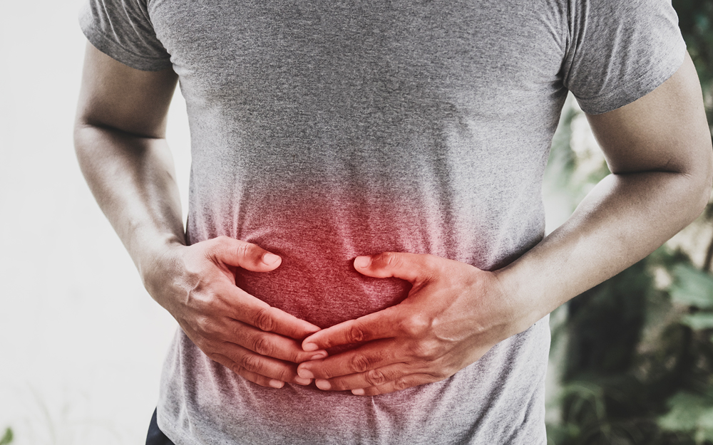 A young Hispanic man holding his stomach worried about having stomach cancer.