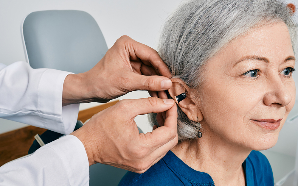 Senior woman during installation hearing aid into her ear by her audiologist, close-up.
