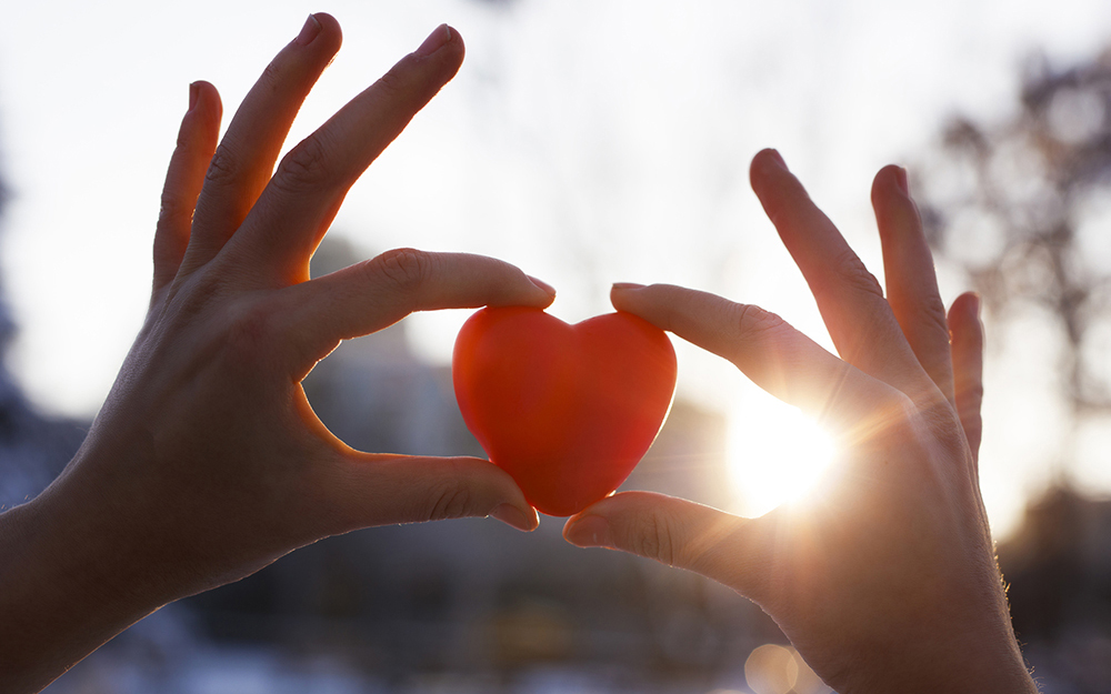 Woman hands holding red heart at sunset