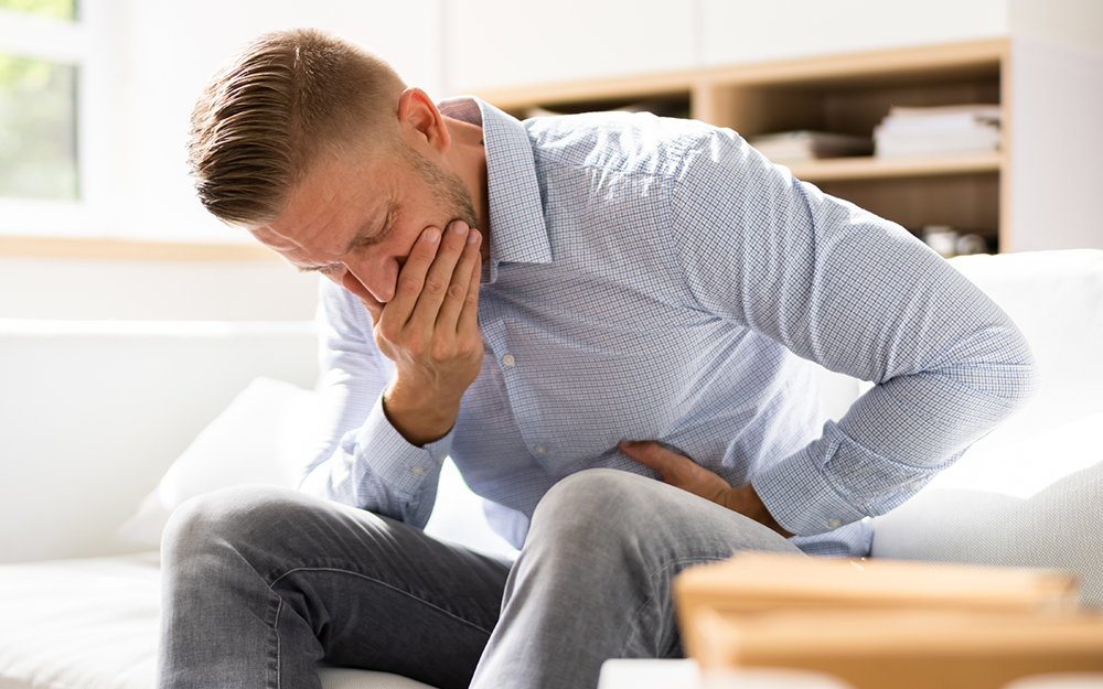 A man sitting on a couch feeling nauseous and throwing up after smoking marijuana.