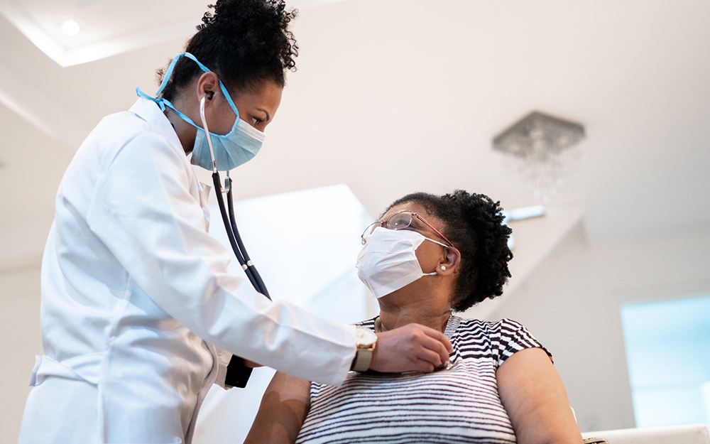 Doctor listening to patient's heartbeat during home visit - wearing face mask