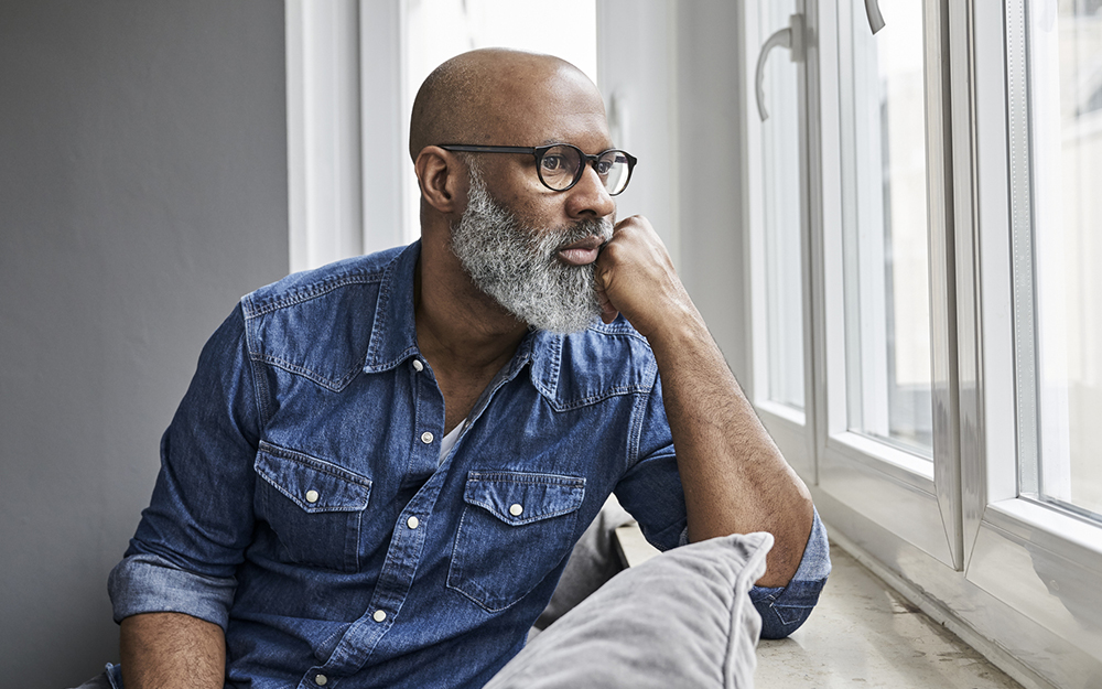 Mature man sitting at window, looking worried 