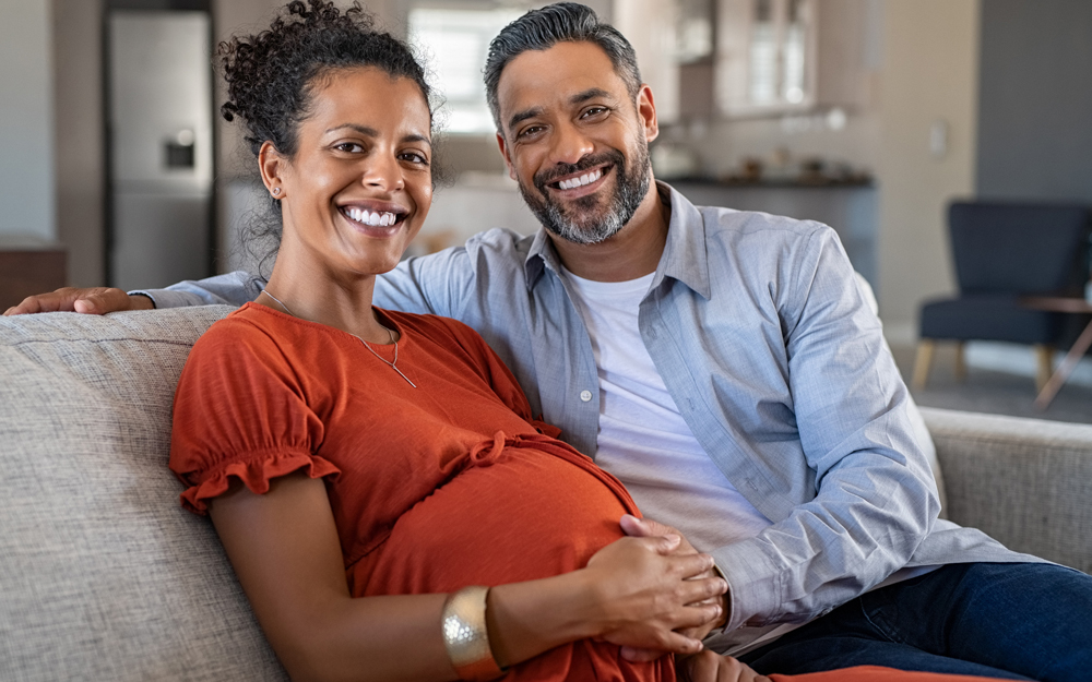 An older couple expecting a baby sitting together on a couch. 