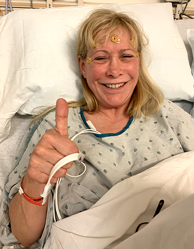 Cedars-Sinai patient Julie Hunter in the hospital giving a thumbs up after experiencing a thunderclap headache.