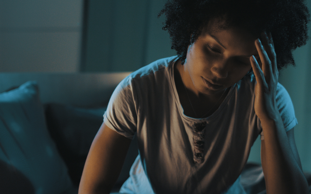 A woman sitting on her bed awake because of a sleep disorder.