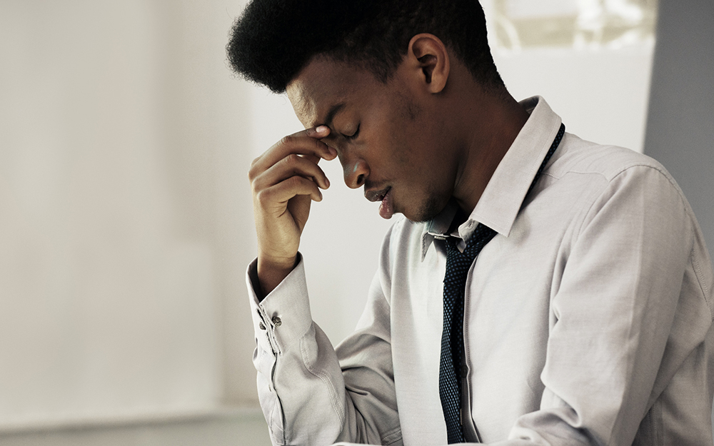 Black male holding his forehead suffering a migraine headache.