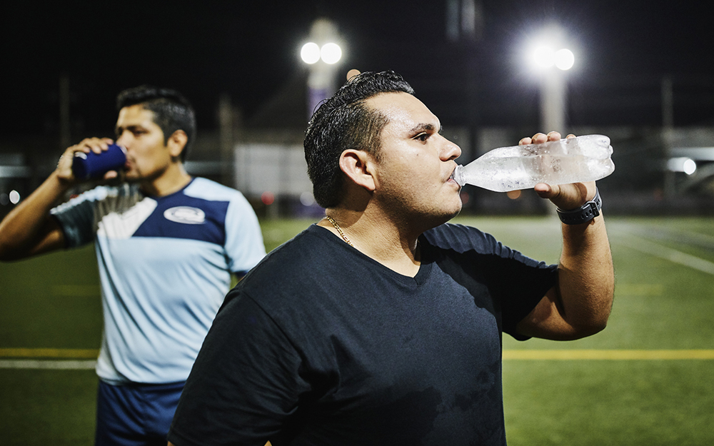 Male soccer player drinking water after nighttime game with friends
