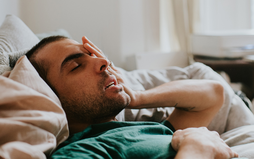 A young man lying in bed feeling fatigued from long COVID.