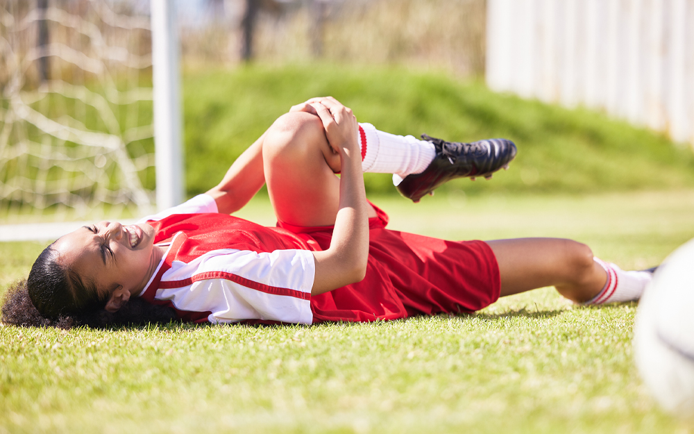 A young woman footballer holding injured knee