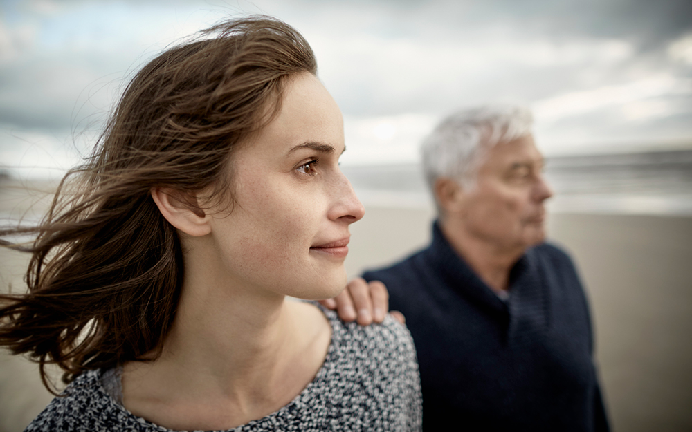 Daughter walking with elderly father on the beach