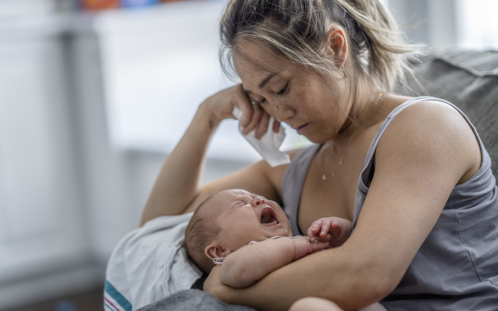 A tired mom trying to breastfeed crying baby