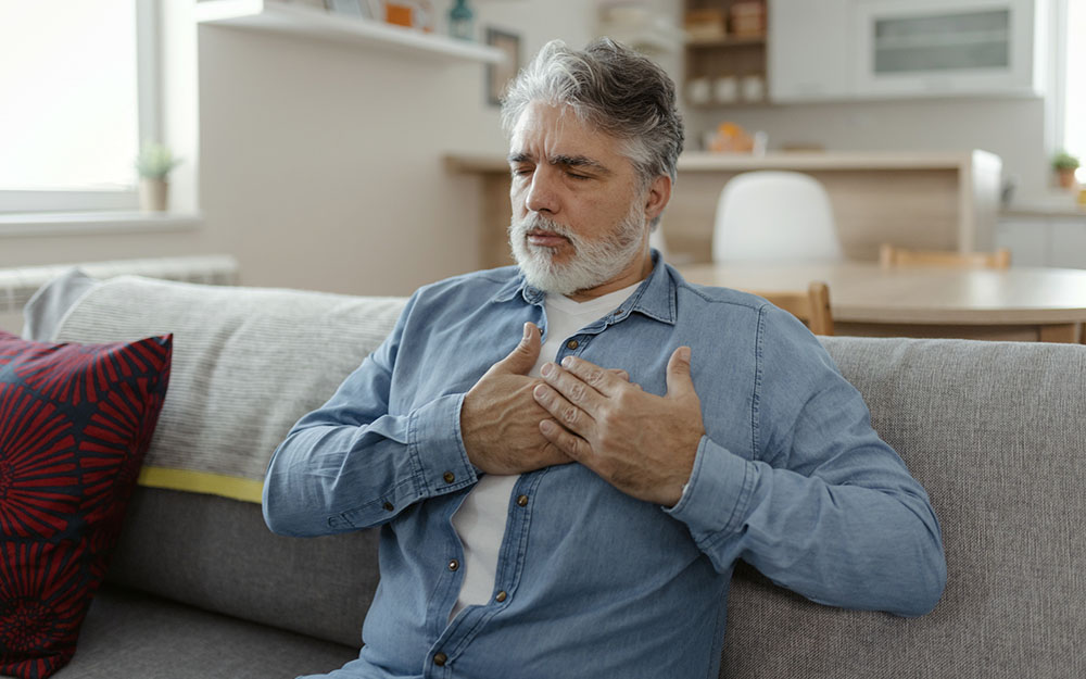 Older man sitting on couch with his hands over his chest.