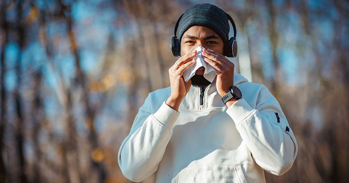 Man with headphones on blowing his nose.