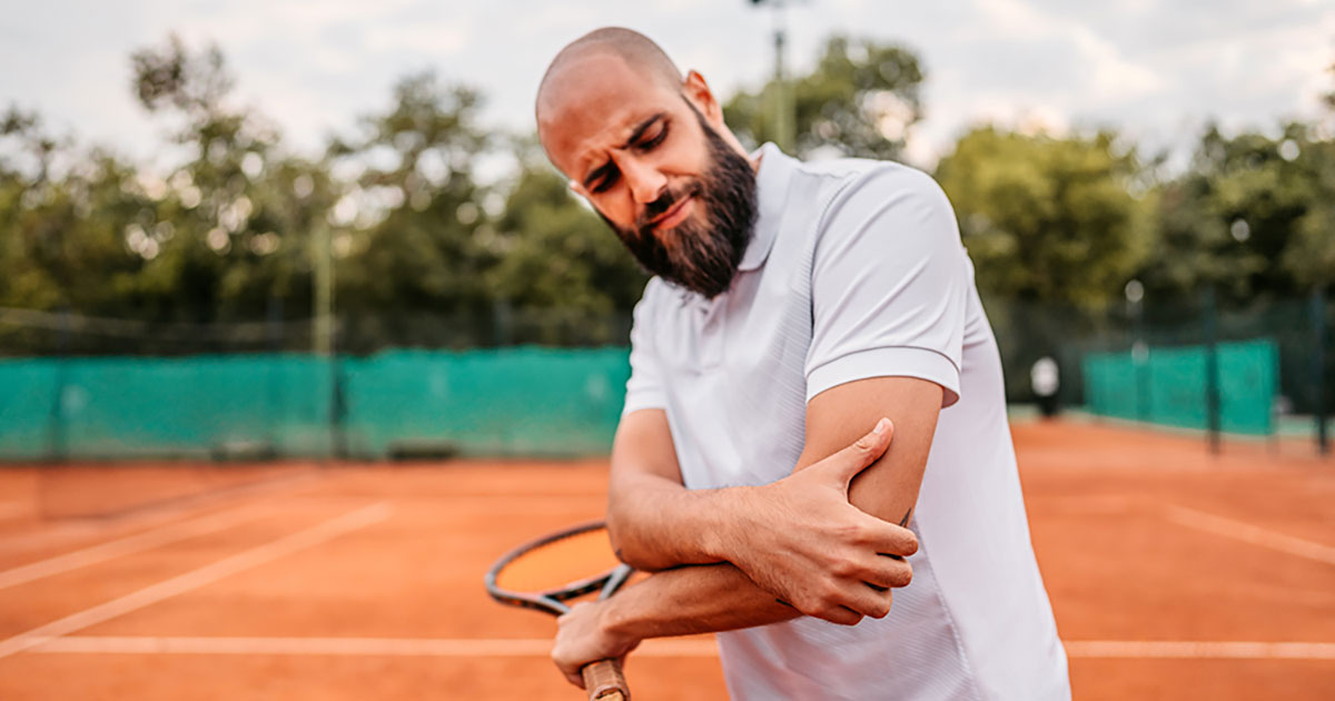 Man on a tennis court holding his elbow.