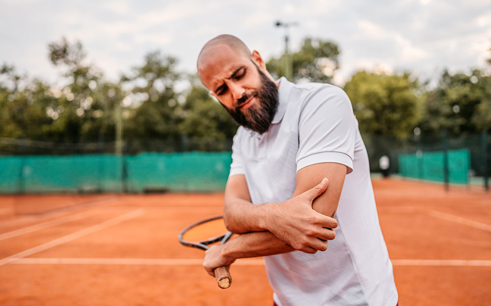 Man on a tennis court holding his elbow.