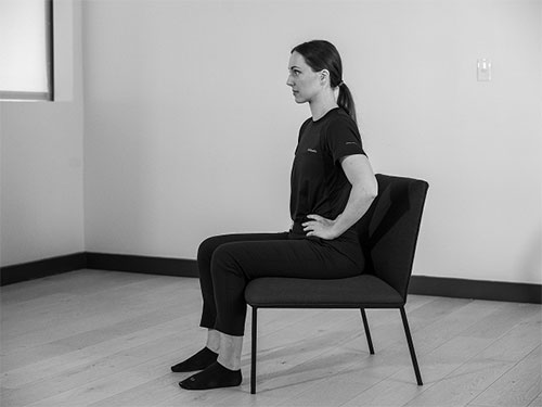 Woman sitting on a shair with her arms on her side.