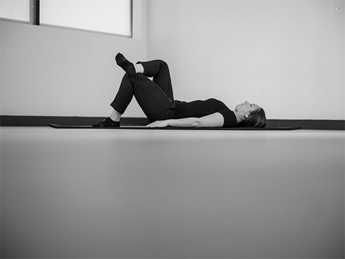 Woman lying on her back and places right ankle on left knee.