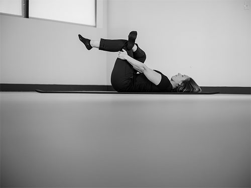 Woman lying on back pulling legs towards her chest.