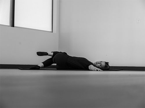 Woman lying on her back with her legs crossed stretching her side.