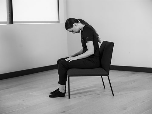 Woman sitting up on chair maintaining good posture looking down.