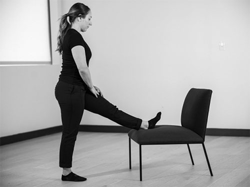 Woman places one heel on the seat of a stationary chair.