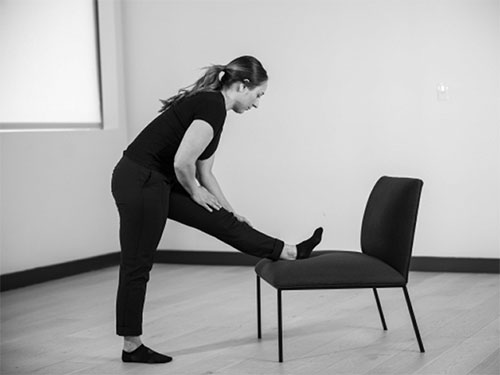 Woman places one heel on a chair, folding her torso forward toward the raised leg.
