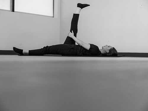 Woman lying on her back with legs out straight, pull one knee toward your body.