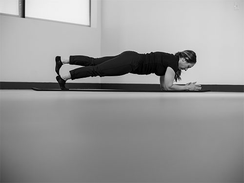 Woman with elbows and forearms on the ground, engage the core and lift up one leg.