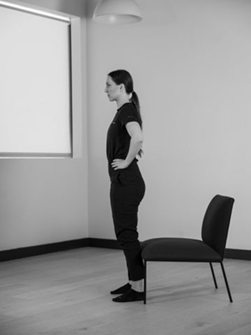 Woman standing upright in front of a chair.