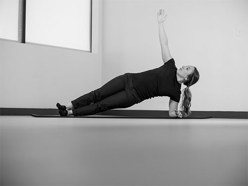Woman performing a side plank with one arm pointing to the ceiling.