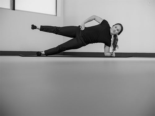 Woman performing a side plank on with her leg raised.