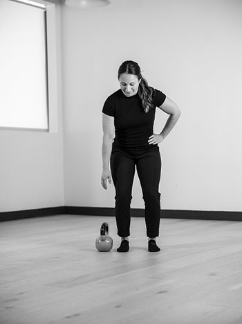 Woman standing with one arm on her side, reaching down.