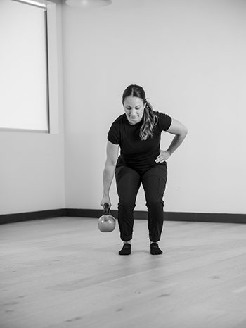 Woman starting to stand up with kettle bell in her hand.
