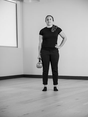 Woman standing upright holding a kettle bell in her hand.