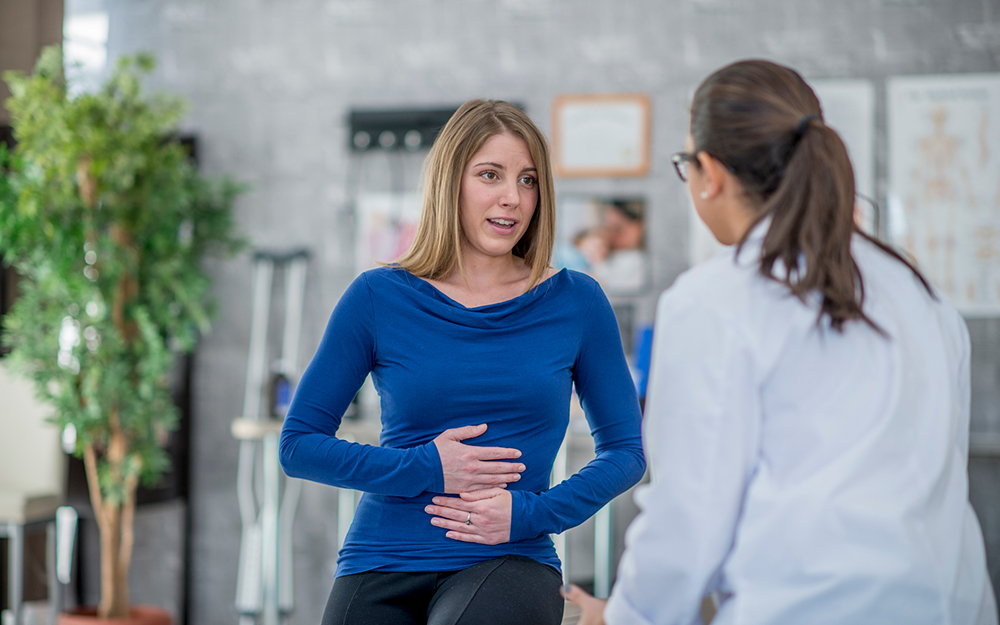 Woman holding her stomach and speaking with her doctor.